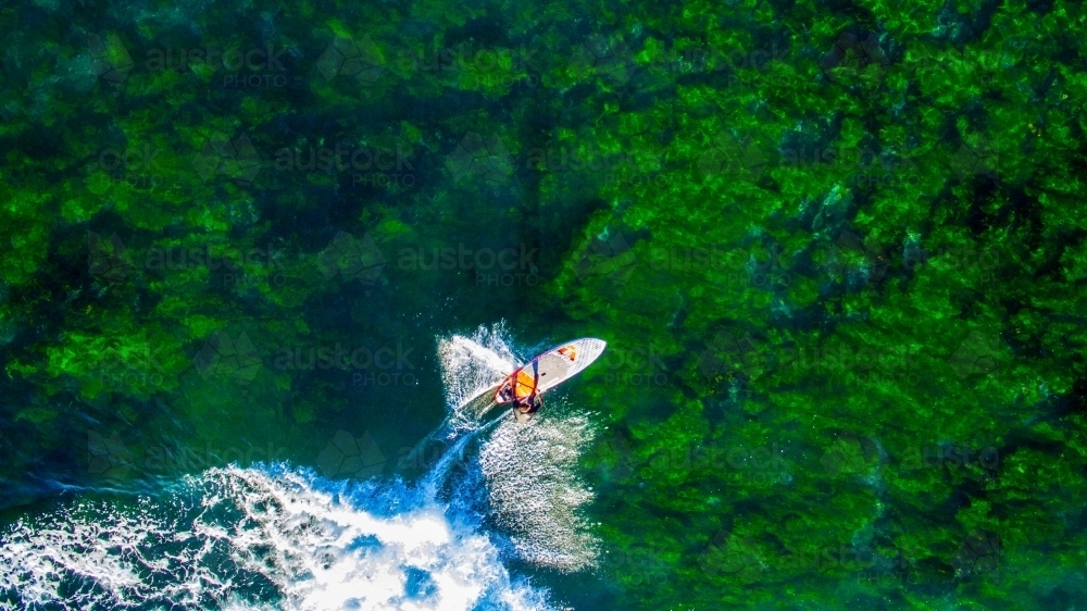 Aerial view of man riding a SUP standup paddle board at Sandon Point - Australian Stock Image
