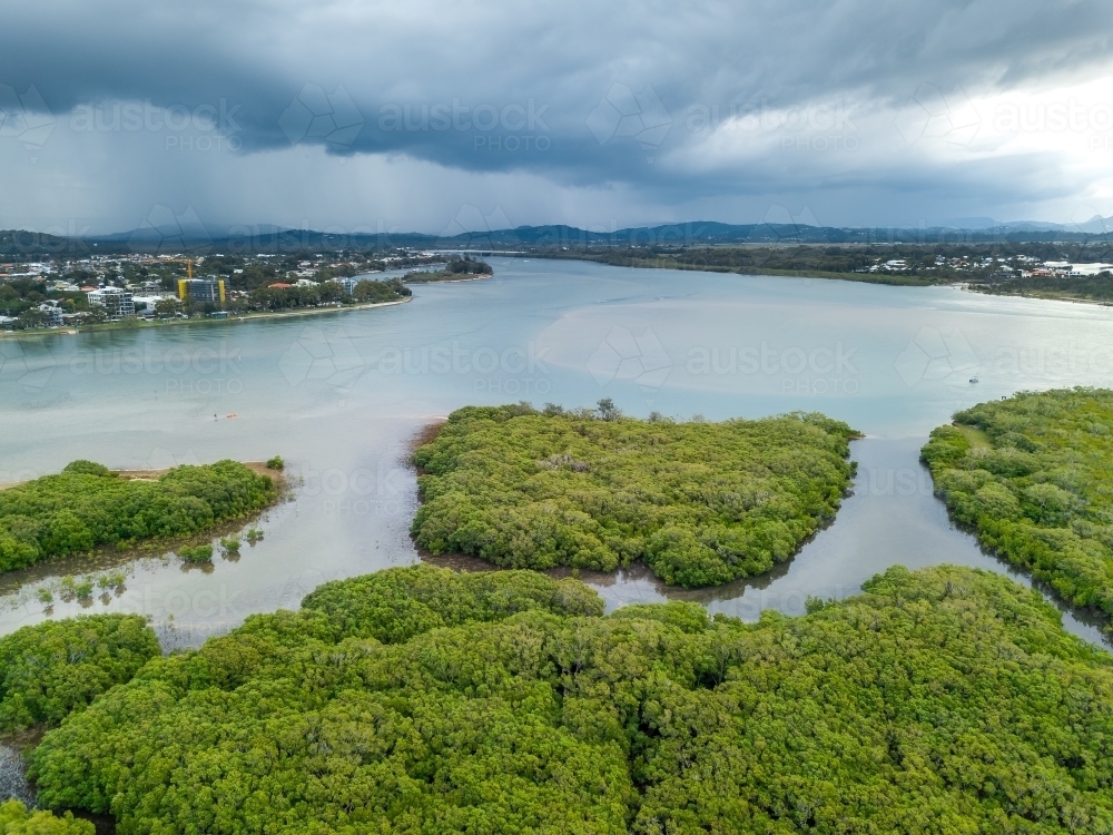 Aerial view of mangroves in a tidal river under dark storm clouds - Australian Stock Image