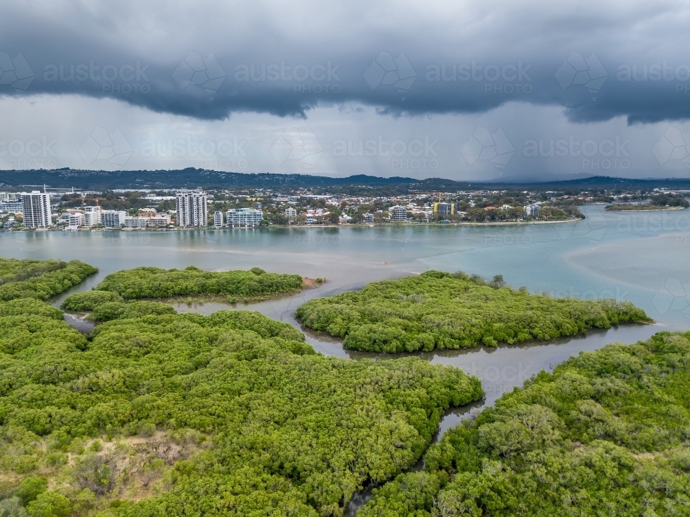 Aerial view of mangroves in a tidal river under dark storm clouds - Australian Stock Image