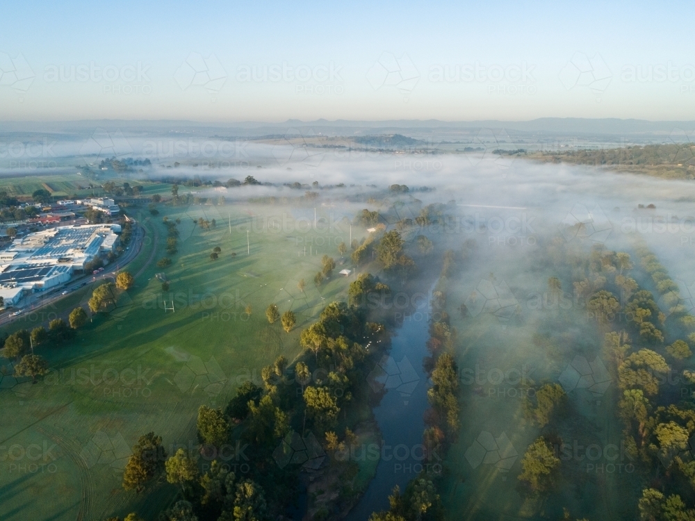 Aerial view of mist over river and parkland beside levee bank to town - Australian Stock Image