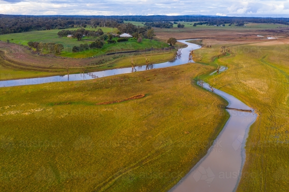Aerial view of narrow rivers flowing towards the horizon through lush farmland - Australian Stock Image