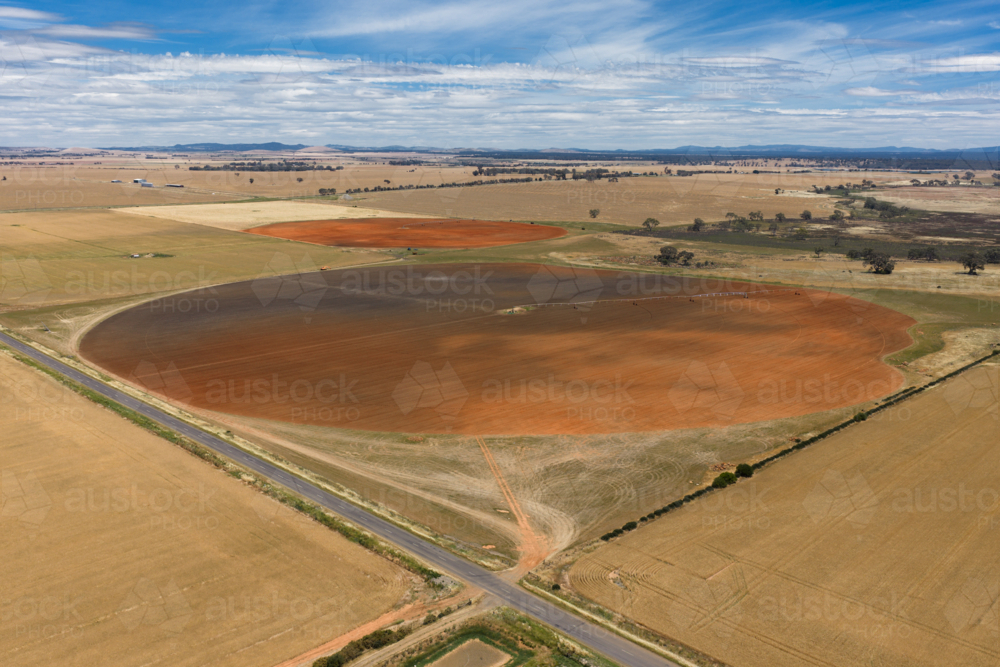 Aerial view of ploughed circular paddock alongside a country road under a blue sky - Australian Stock Image