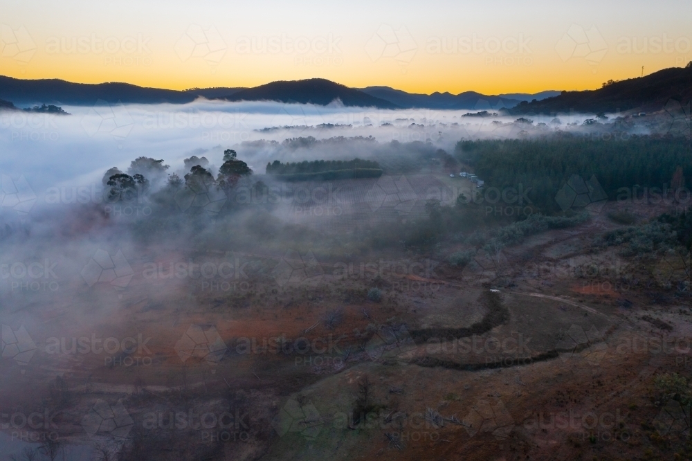 Aerial view of pre dawn lighting over a rural valley covered in fog - Australian Stock Image