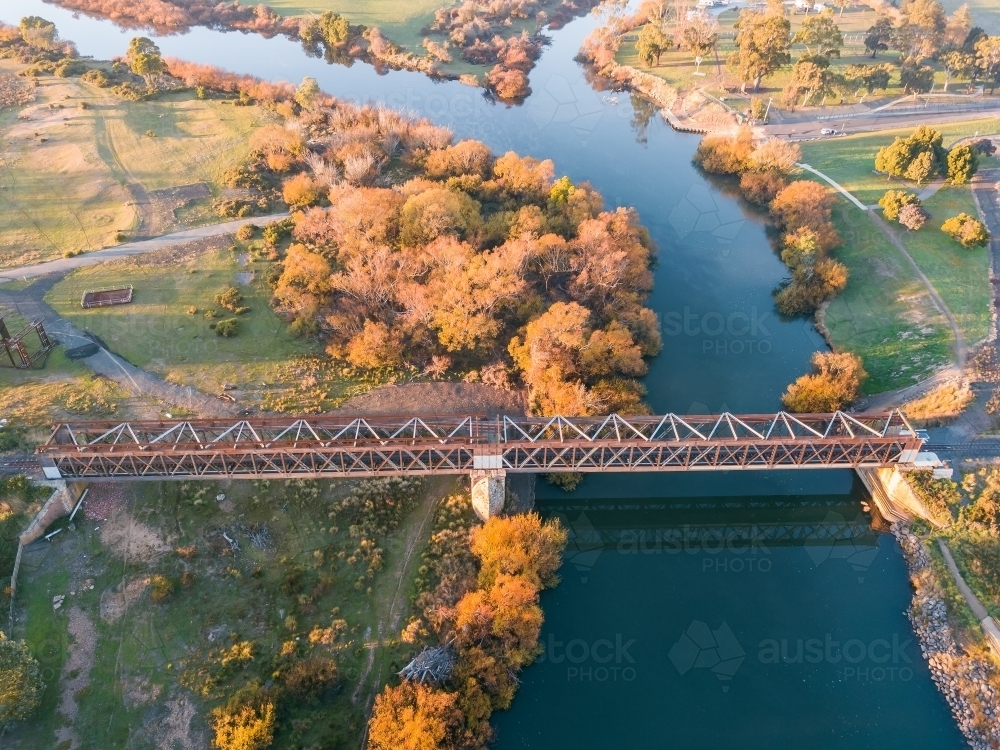 Aerial view of railway bridge spanning a river lined with Autumn trees - Australian Stock Image