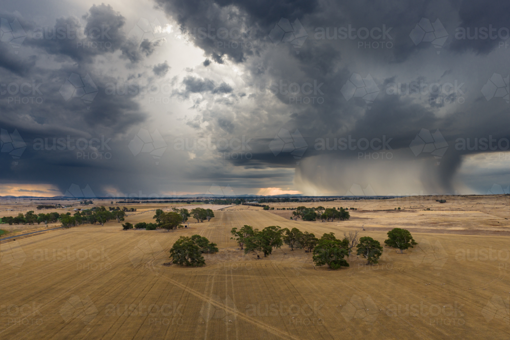 Aerial view of rain falling from dramatic storm clouds over a dry farmland - Australian Stock Image