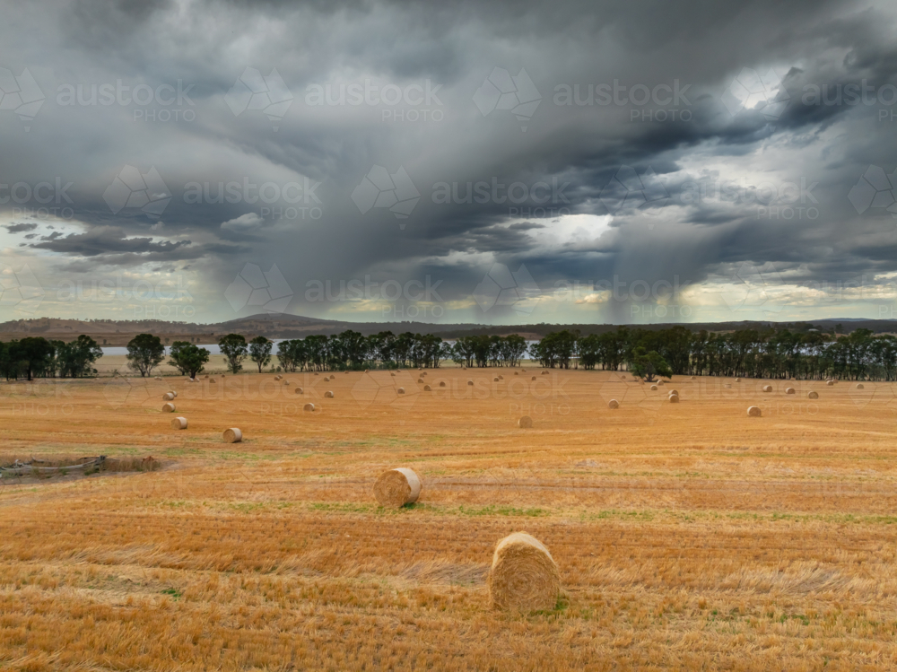 Image of Aerial view of rain showers falling from dark clouds over hay