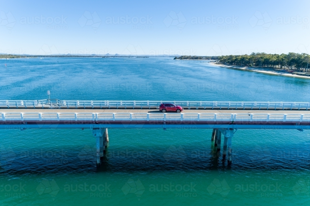 Aerial view of red car on bridge over water. - Australian Stock Image