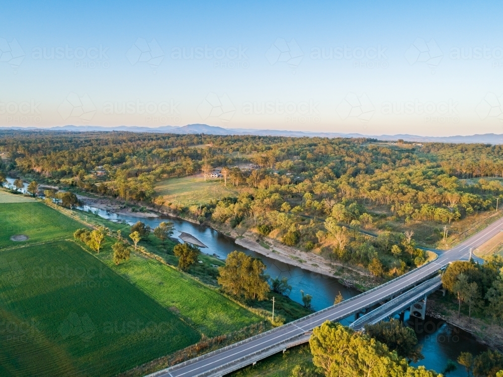 Aerial view of road and bridge over floodplain farmland in sunset light - Australian Stock Image