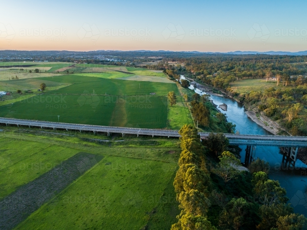Aerial view of road and bridge over floodplain farmland in sunset light - Australian Stock Image
