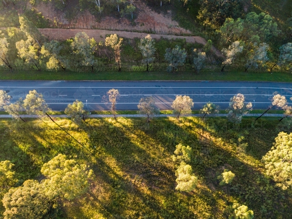 Aerial view of road through undeveloped land with trees and footpath alongside it - Australian Stock Image