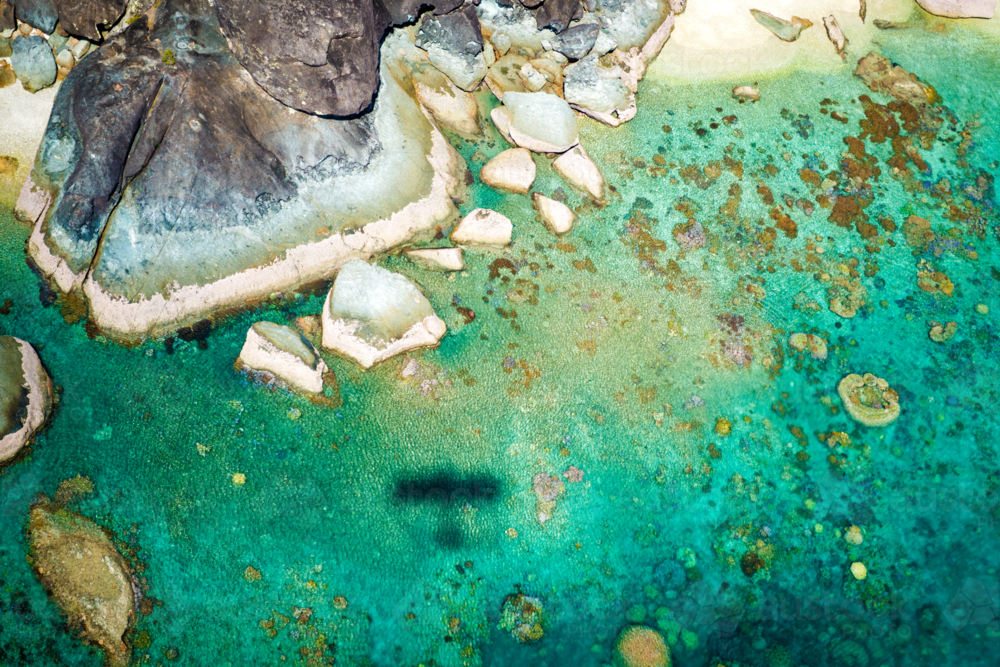 Aerial view of rocky shoreline and coral reef in clear tropical water with plane shadow. - Australian Stock Image