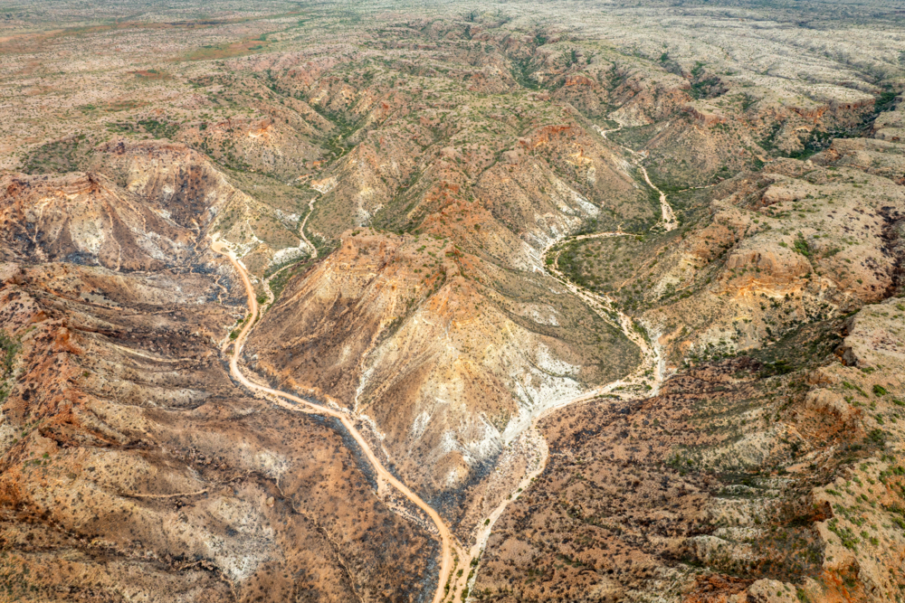 Aerial view of rugged arid gorges and ridges with a winding dirt track through remote ranges - Australian Stock Image