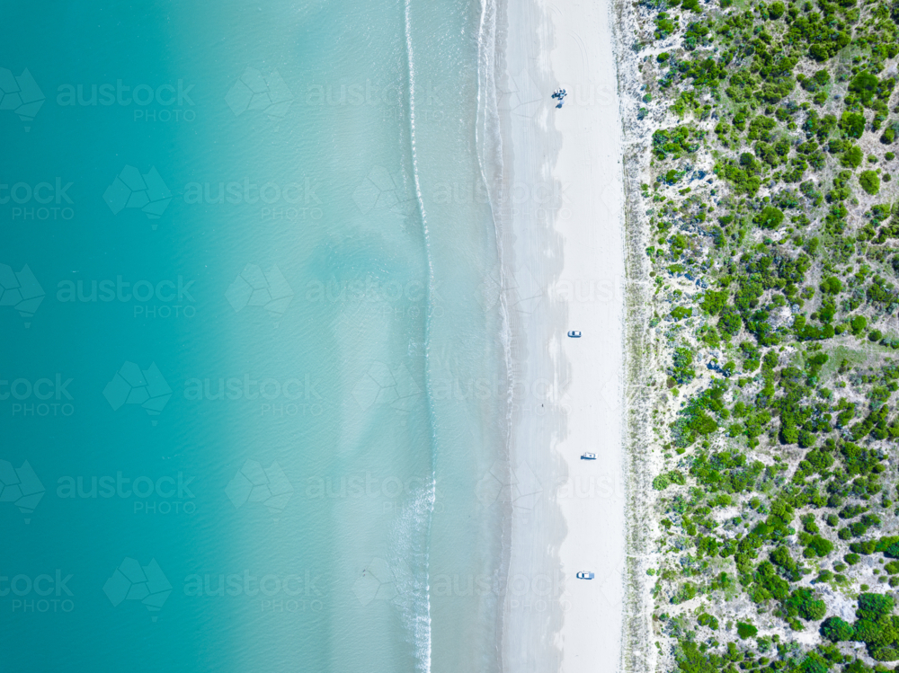 Aerial view of sandy white beach and turquoise ocean water beside coastal vegetation - Australian Stock Image