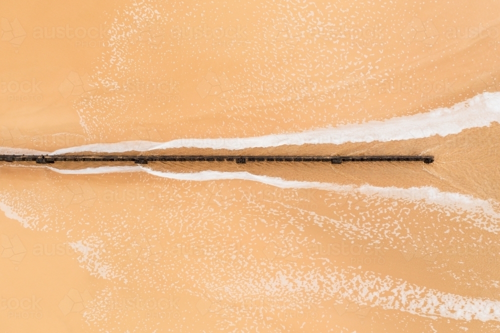 Aerial view of seawater rushing past a wooden groyne on a sand beach - Australian Stock Image