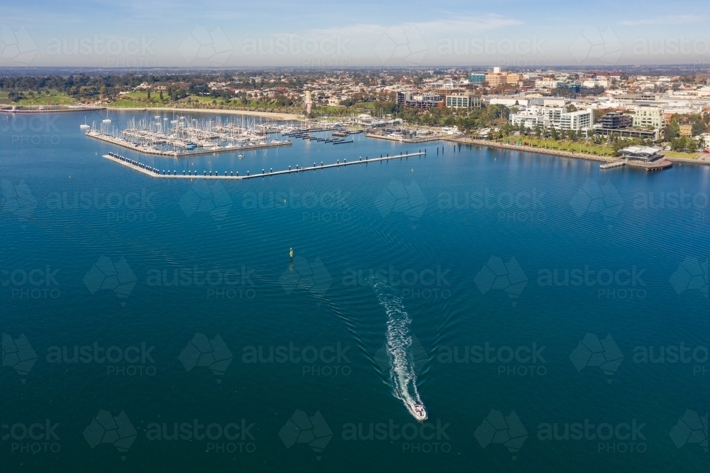 Aerial view of small boat on a blue coastal bay with a marina and city in the background - Australian Stock Image