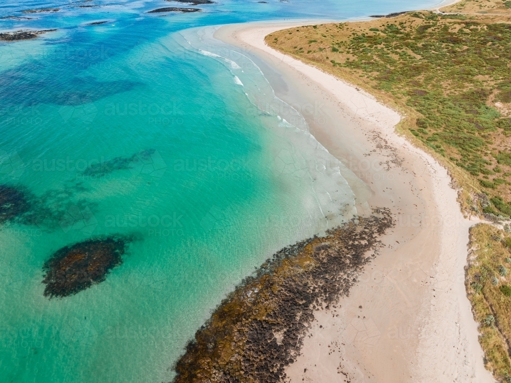 Aerial view of small rocky reefs in turquoise blue water off a white sandy beach - Australian Stock Image