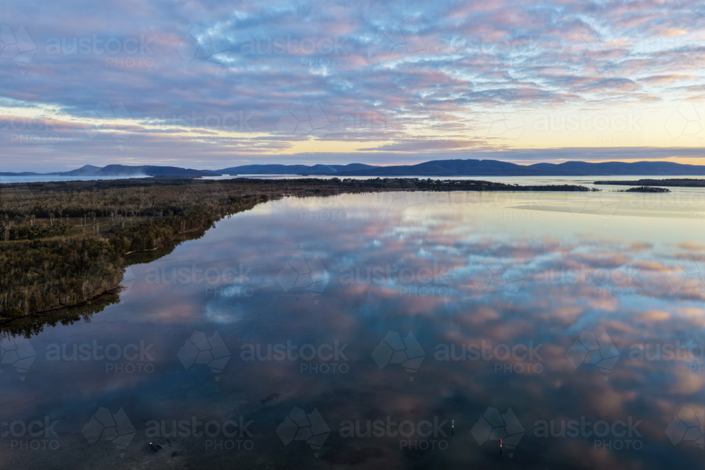 Aerial view of soft pastel clouds reflected across the calm waters of Pipers Bay - Australian Stock Image