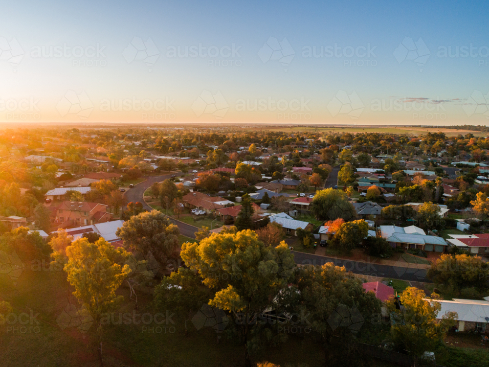 Aerial view of sun on horizon casting warm glow over homes in housing area of Dubbo at sunset  - Australian Stock Image