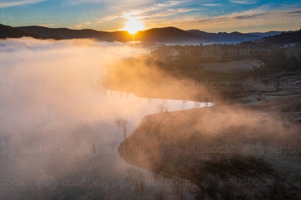 Aerial view of sunrise over mountains surrounding a lake covered in fog - Australian Stock Image