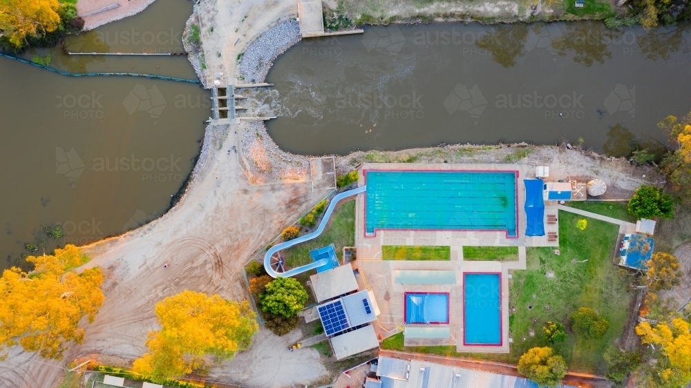 Aerial view of swimming pool complex along side a a river flowing through a flood gate - Australian Stock Image