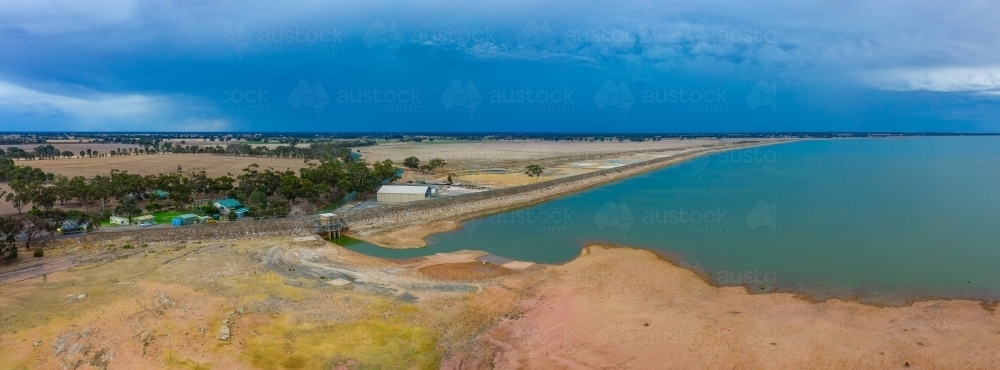 Aerial view of the dam wall of large reservoir with dark clouds overhead - Australian Stock Image