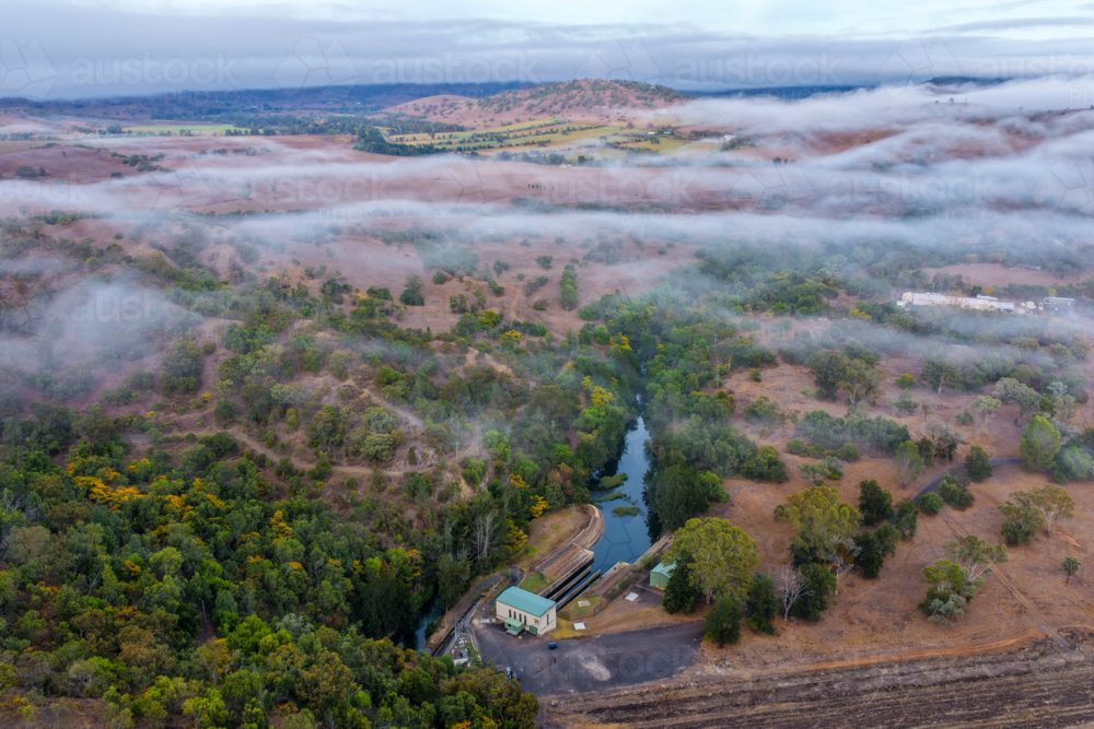 Aerial view of the Glenbawn Dam valve house with fog rolling through the surrounding valley - Australian Stock Image