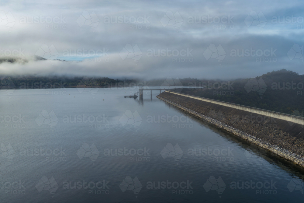 Aerial view of the Glenbawn Dam wall and surrounding landscape with fog rolling through the valley - Australian Stock Image