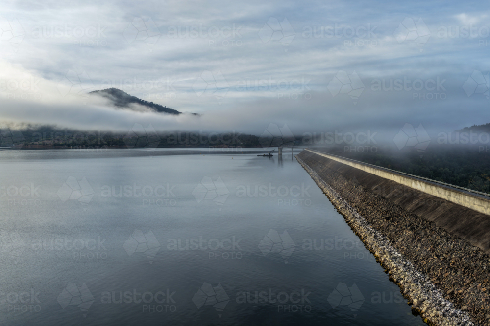 Aerial view of the Glenbawn Dam wall and surrounding landscape with fog rolling through the valley - Australian Stock Image