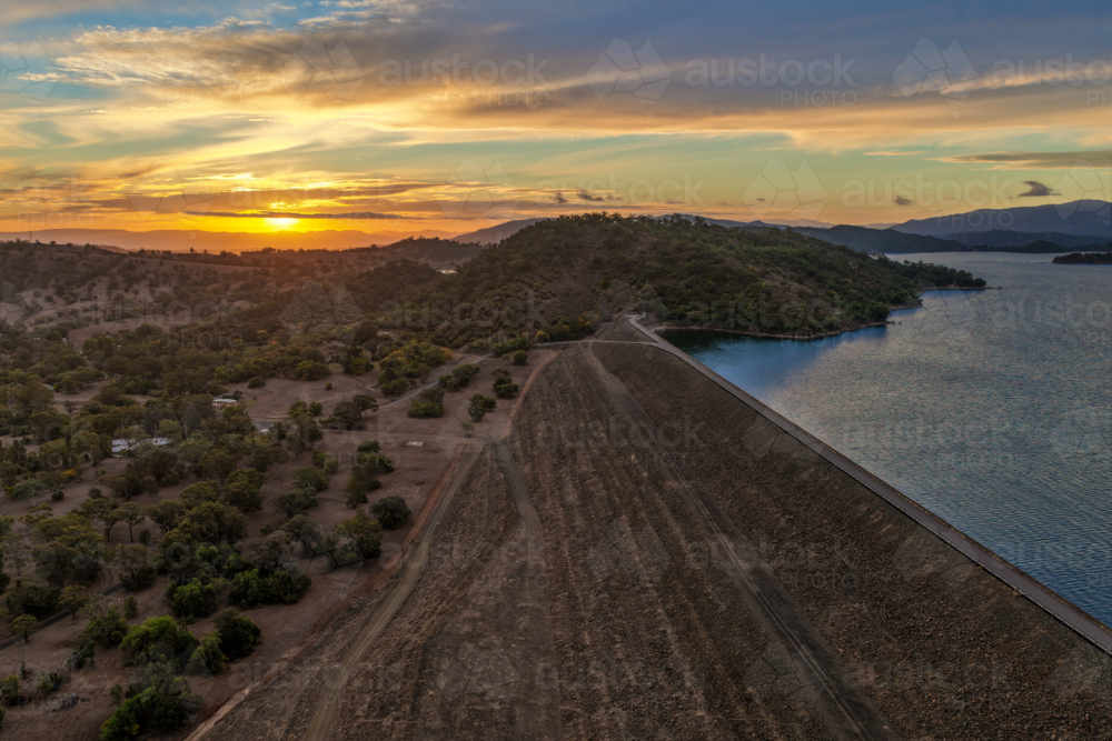 Aerial view of the Glenbawn Dam wall leading towards a sunset over the surrounding mountain range - Australian Stock Image