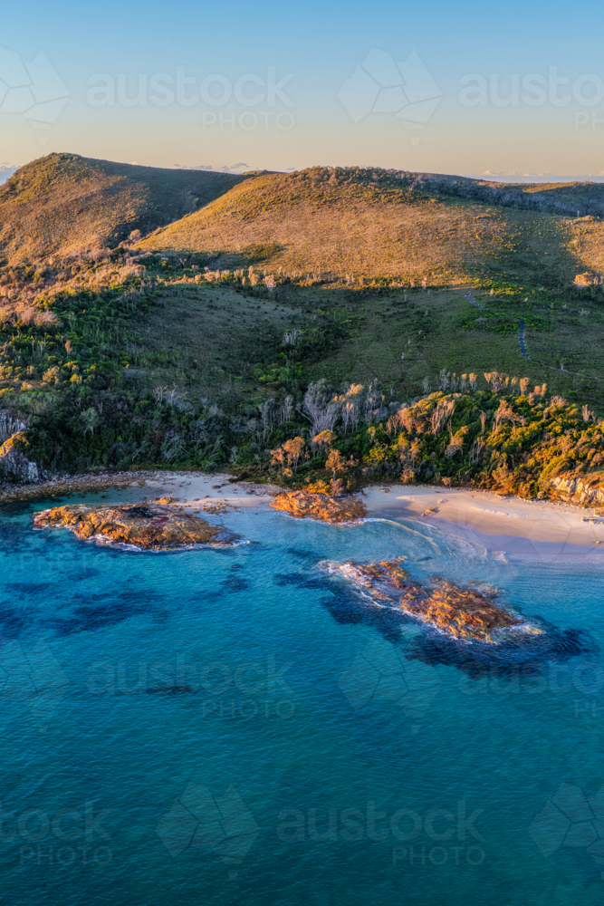 Aerial view of the rugged rocky headland at Diamond Head surrounded by clear turquoise ocean water - Australian Stock Image