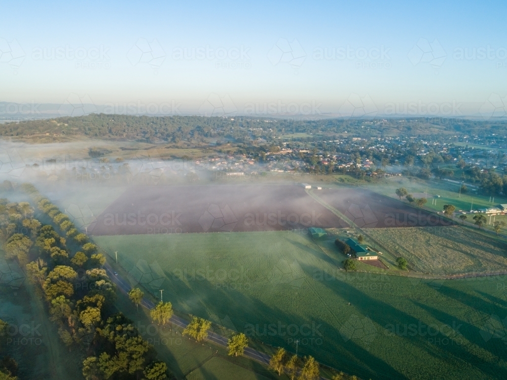 Image of Aerial view of thin fog over green and brown farm paddocks at ...