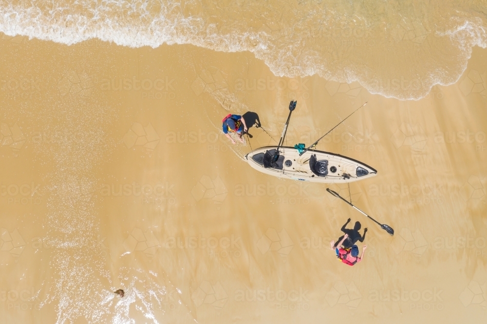 Aerial view of two people launching a kayak on a beach - Australian Stock Image