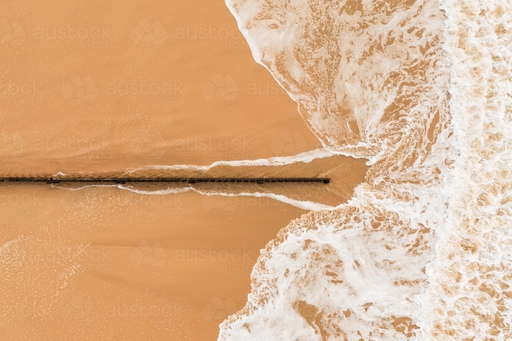 Aerial view of waves approaching a wooden groyne on a sand beach - Australian Stock Image