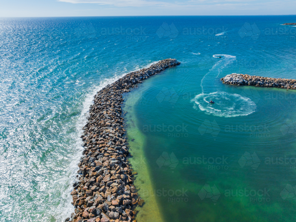 Aerial view of waves breaking on a long rocky breakwater surrounding a marina - Australian Stock Image