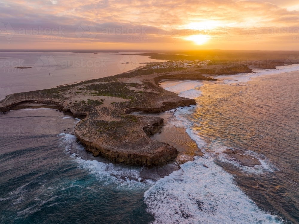 Aerial view of waves crashing against eroded cliffs along a rugged coastline at sunrise - Australian Stock Image