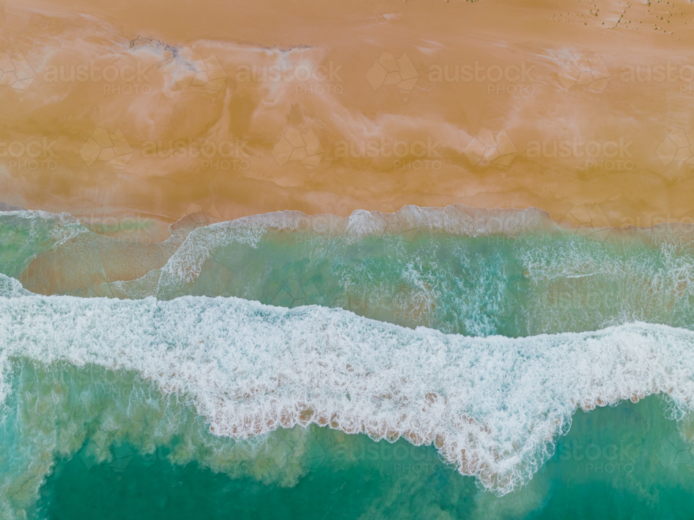 Aerial view of waves crashing on a a golden sandy beach - Australian Stock Image