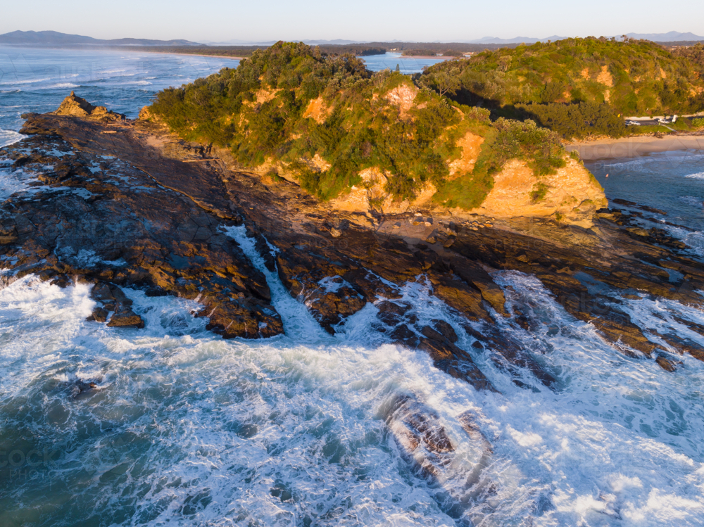 Aerial view of waves crashing on large rocky outcrop in golden morning light - Australian Stock Image