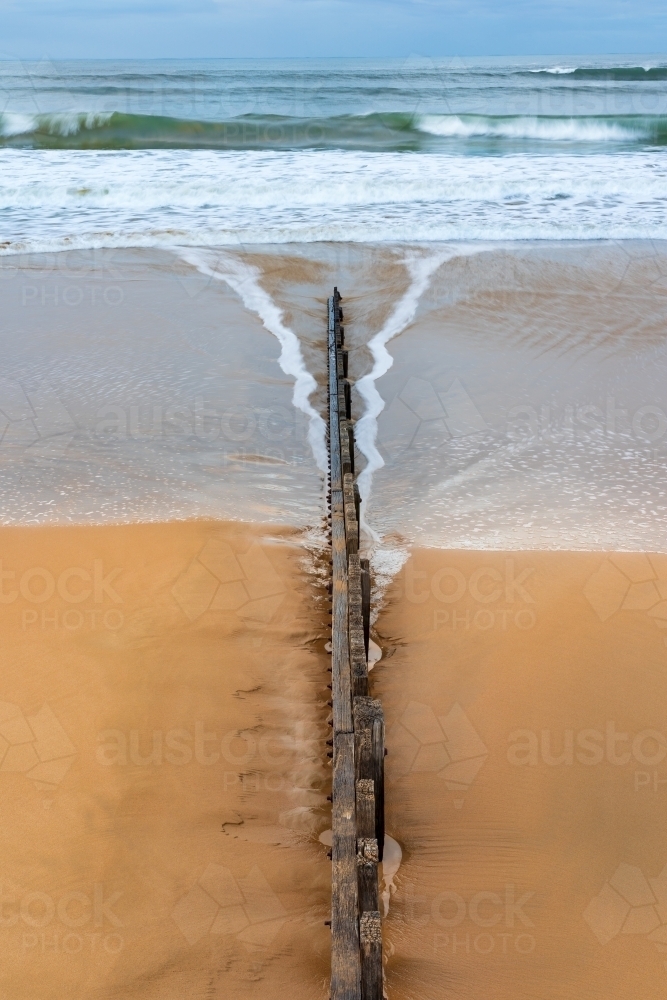 Aerial view of waves receding past a wooden groyne on a sandy beach - Australian Stock Image