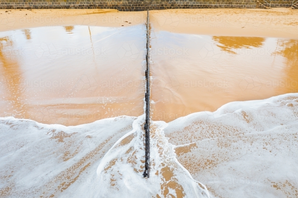 Aerial view of waves rushing past a wooden groyne on a sand beach - Australian Stock Image