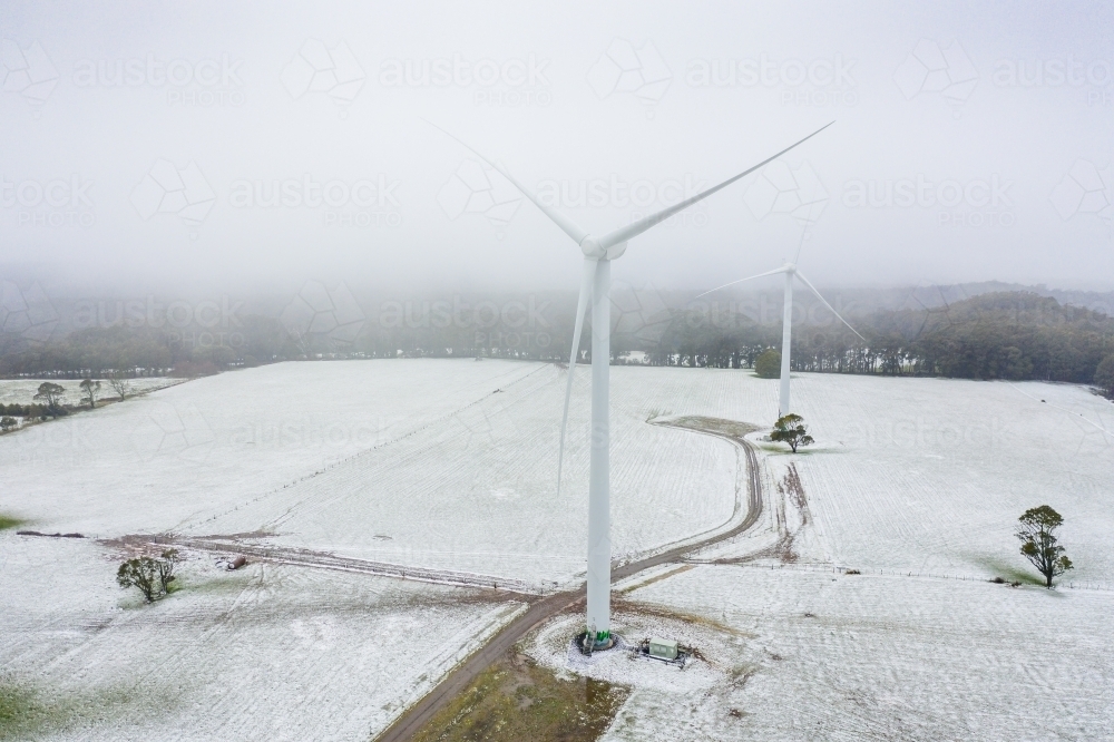 Aerial view of wind turbines in a foggy sky on a snow covered hilltop - Australian Stock Image