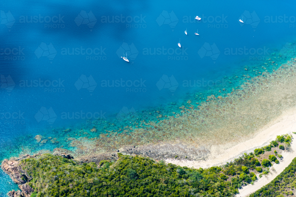 Aerial view of yachts anchored near a coral reef and tropical shoreline - Australian Stock Image
