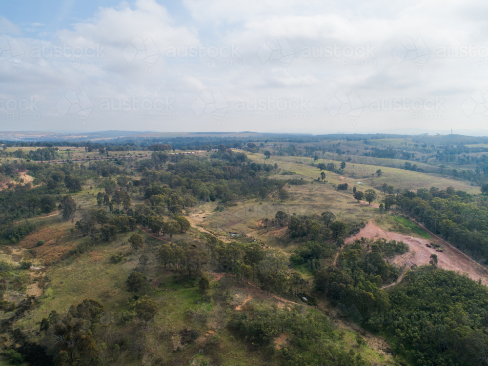 Aerial view on hazy day of unused land at edge of town with bike trails through paddock - Australian Stock Image