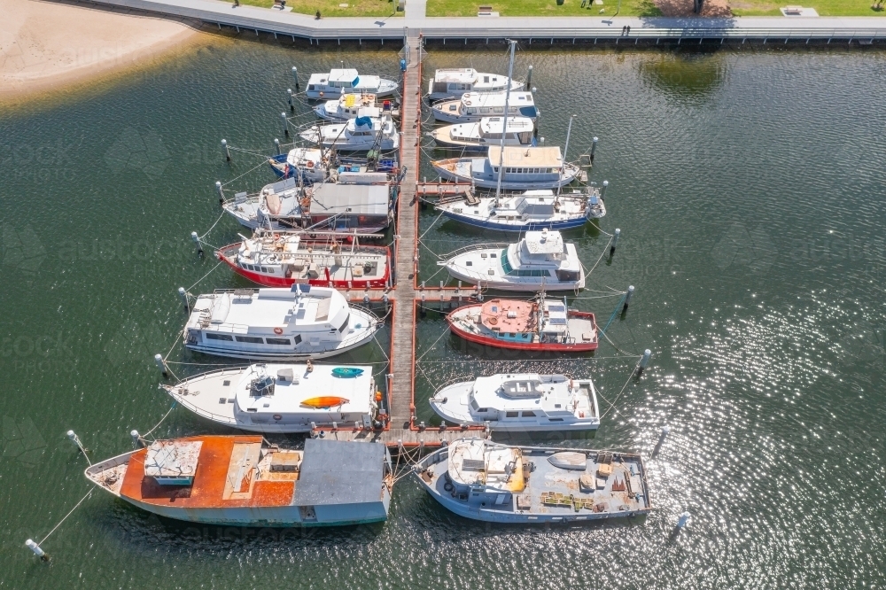 Aerial view over a fleet of fishing trawlers lined up and moored along a jetty - Australian Stock Image