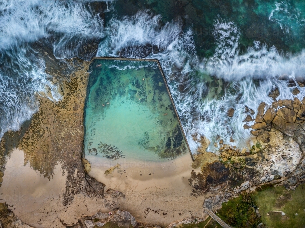 Aerial views  odd shaped rock pool with waves surging around it - Australian Stock Image