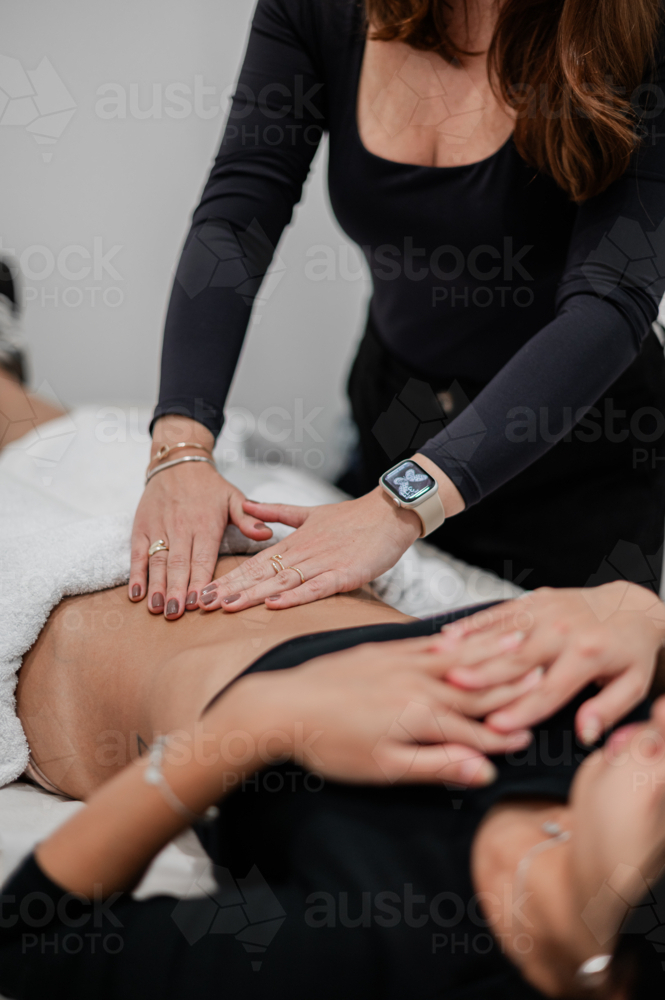Aesthetic practitioner assessing clients abdomen while lying on a treatment bed - Australian Stock Image