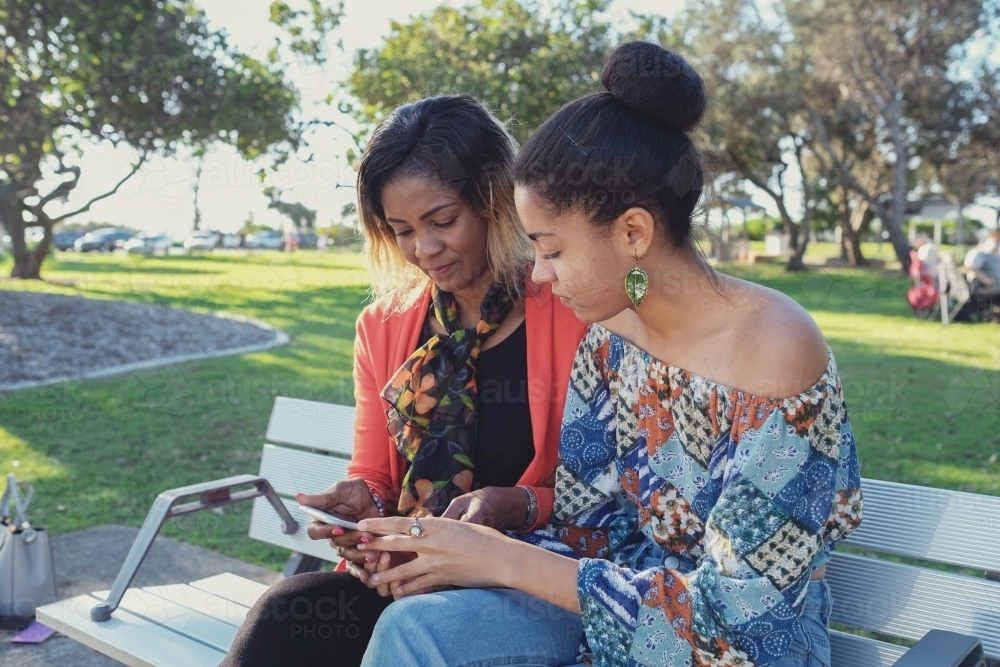 African mother and multicultural teen daughter using mobile phone - Australian Stock Image