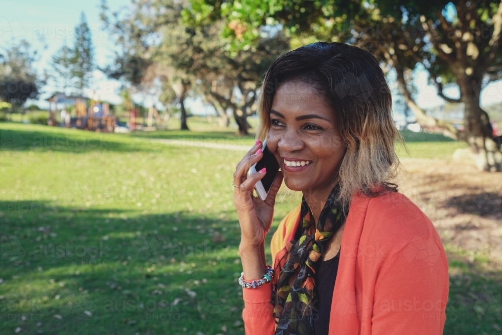 African woman on the phone in the park - Australian Stock Image