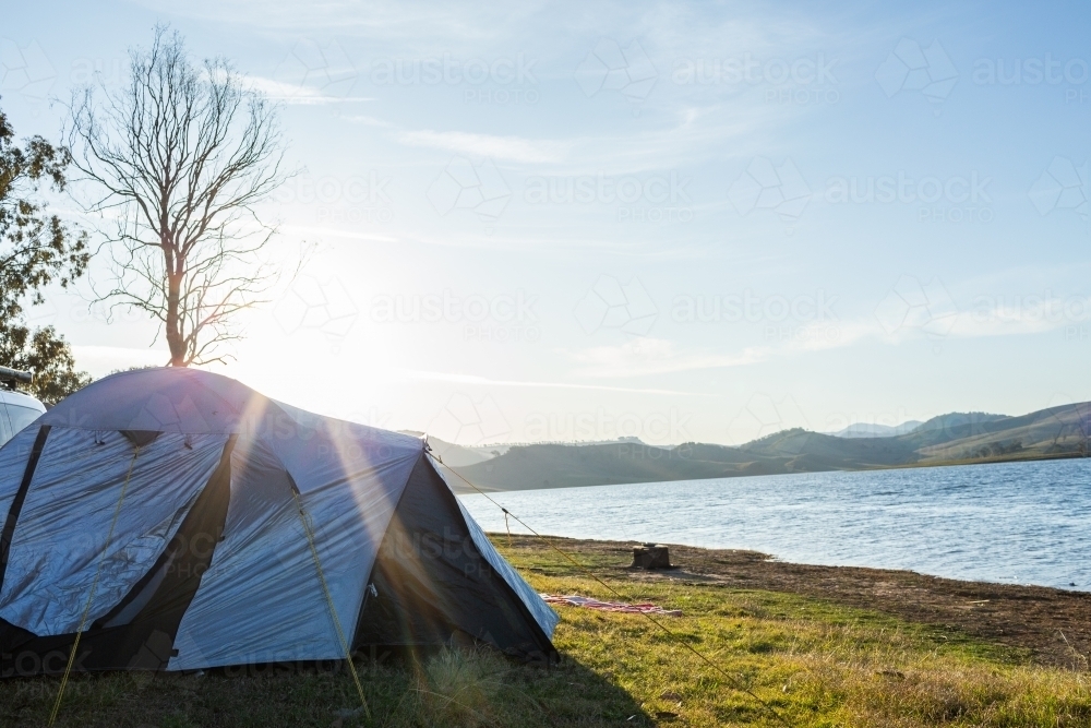 Afternoon Sun flare over tent pitched by edge of Lake St Clair in Hunter Valley - Australian Stock Image