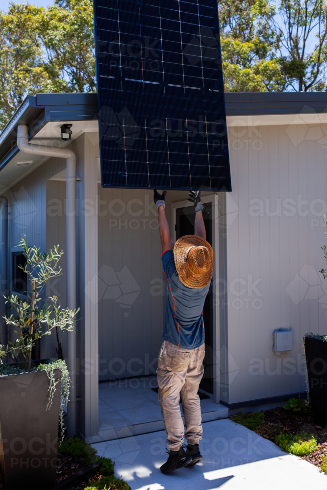 All black bifacial solar panel lifted up on hot roof of Australian home during installation job - Australian Stock Image
