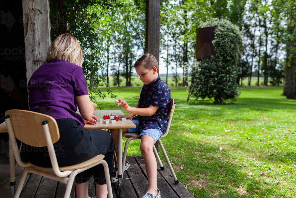 allied health professional speech therapist working with boy in rural location on farm verandah - Australian Stock Image